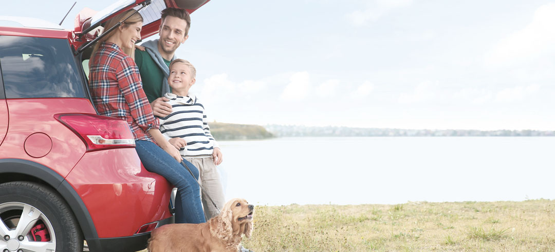 Familia contenta apoyada en el maletero de un coche con su perro y el mar de fondo